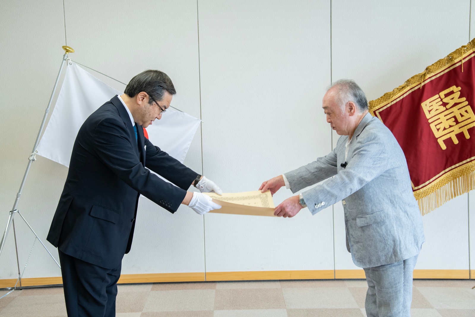 山下学長から東原様に紺綬褒章の章記が伝達される様子
