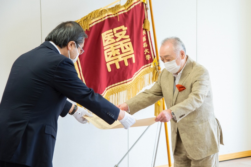 山下学長から東原様に紺綬褒章の章記が伝達される様子