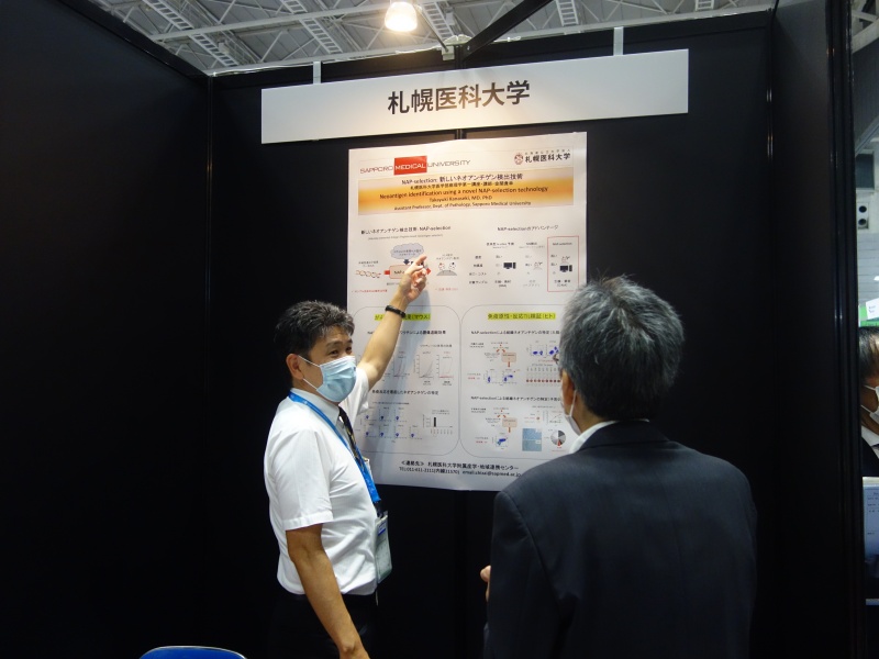 本学展示ブースへの来場者に研究内容を説明している様子