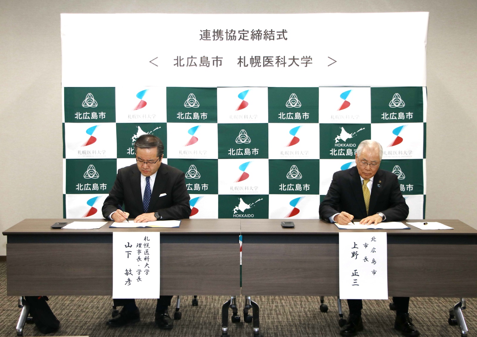 北広島市の上野市長と本学の山下理事長・学長が協定書に署名しています。